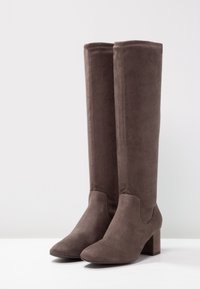 Botas altas de ante marrón hasta la rodilla con un tacón bloque, que presentan una textura suave y una punta redondeada, diseñadas con acentos de costura mínimos.