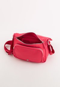 Bolso bandolera de nylon rosa con un compartimento principal con cremallera, un bolsillo frontal con cremallera y una correa ajustable. Textura suave, forma rectangular.