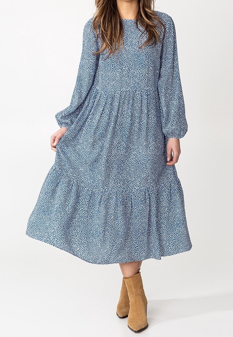 Blau gemusterte Kleid mit langen Ärmeln, geraffter Taille und gestaffeltem Saum; getragen mit hellbraunen Knöchelstiefeln. Verfügt über einen dezenten Punkten-Print.
