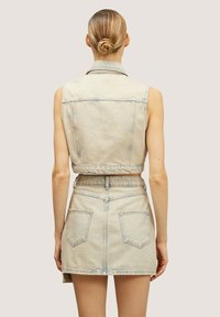 Ljust tvättad denimväst och kjolset. Har en kortad design, synlig sömnad och två bakfickor på kjolen.