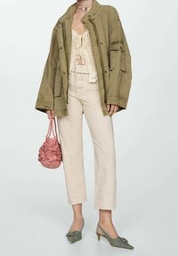 Olijfgroen oversized jack, crèmekleurig haaktop met strikjes, lichtbeige rechte broek, groene hakken en een roze textuur tas.