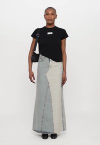 Black short-sleeve t-shirt with a small logo, paired with a light blue denim maxi skirt featuring a distinctive asymmetrical seam and contrast panels.