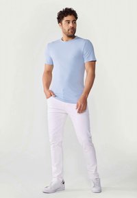 Cameră cu un tricou scurt, de culoare albastru deschis, asortat cu blugi albi. Tricoul are un decolteu rotund, iar ținuta include teniși albi.