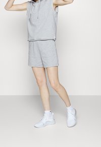 Haut sans manches gris clair avec cordon de serrage, associé à un short assorti. Porté avec des chaussures de sport blanches et des chaussettes mi-mollet.