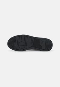 Černá podešev sportovní obuvi se strukturovanými vzory, obsahující logo Puma a různé vzory dezénu. Gumový materiál s plochým tvarem.