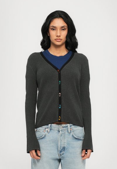 Gray ribbed cardigan with long sleeves, black trim, and colorful buttons. Worn over a blue top with textured detailing and loose-fitting light jeans.