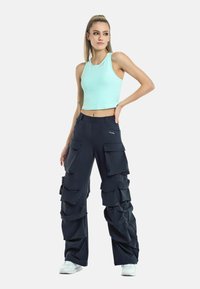 Light blue cropped tank top, paired with dark cargo pants featuring multiple pockets and a loose fit. White athletic shoes.