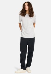 Grijze katoenen t-shirt met korte mouwen en logo, gecombineerd met losse zwarte broek en lichte sneakers; minimalistisch ontwerp en casual pasvorm.