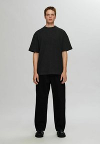 Svart ribbad stickad oversize t-shirt med korta ärmar, kombinerad med löst sittande svarta byxor och strukturerade svarta skor. Enkel bakgrund.