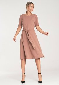 Różowa sukienka w odcieniu blush z krótkimi rękawami, z paskiem w talii i zwiewnym dołem. Wykonana z gładkiego materiału, z okrągłym dekoltem i długości do połowy łydki.