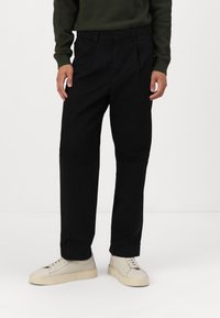 Svarta bomullsbyxor med rak bendesign, prydda med en framficka och bälteshällor, i kombination med beige sneakers.