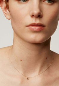 Collar de tono dorado con una delicada cadena y un pequeño colgante en forma de estrella. El tono de piel es claro con sutiles pecas en el cuello.