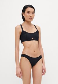 Črn bikini set z oblikovano zgornjim delom bralette z izrezom in nastavljivimi naramnicami, v kombinaciji z bikini spodnjimi hlačkami z nizkim pasom.