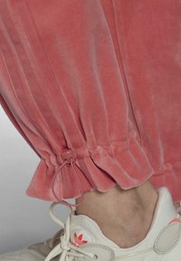 Pink velvet jogger with elastic cuff and drawstring detail at the hem, paired with a white sneaker featuring pink accents.