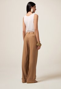 Bruine wijde broek met een textuurafwerking, hoge taille en een opgestikte zoom. Combi met een fitted witte mouwloze top en een gouden armband.