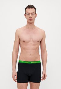 Caleçons boxers noirs avec une ceinture élastique vert fluo portant l'inscription "BJÖRN BORG". Tissu lisse, design ajusté, longueur mi-cuisse.