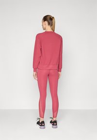 Joga set koji sadrži bordo duksericu i odgovarajuće tajice s mrežastim panelima. Outfiti su izrađeni od rastezljivog, prozračnog materijala.