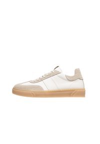 Zapatillas de cuero blancas con acentos de ante beige, punta redondeada, parte delantera con cordones y suela de goma texturizada. Presenta rayas horizontales blancas.