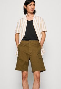 Napapaita, jossa on beige- ja valkoviiruja, musta toppi ja oliivinvihreät cargo-shortsit sivutaskuilla. Silkkinen kangas, rento malli.