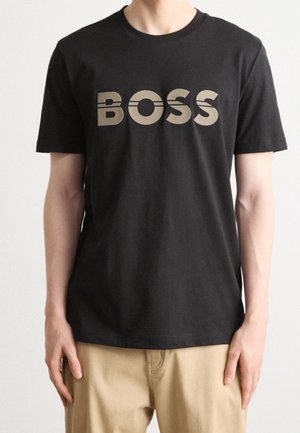 T-shirt en coton noir avec un grand logo "BOSS" beige sur le devant. Manches courtes et col ras du cou classique. Texture lisse.