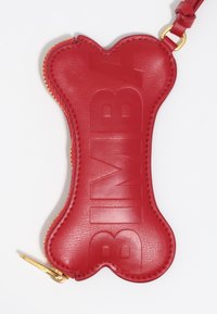 Czerwona skórzana saszetka w kształcie kości z tłoczonym napisem "BIMBA", złotym zamkiem błyskawicznym i skórzanym paskiem do mocowania. Gładka faktura i wyraźne krawędzie.