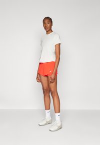 Camiseta atlética de manga corta en gris claro combinada con pantalones cortos naranjas y zapatillas blancas con detalles en gris, presentando un logo de Nike en cada prenda.