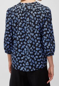 Blusa nera con un motivo floreale in tonalità blu, maniche 3/4, dettagli arricciati sul retro e scollo tondo.