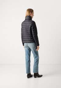 Doudoune noire avec col montant, dotée d'un design matelassé et d'une silhouette ajustée, associée à un jean en denim bleu clair et des bottines noires.
