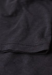 Primer plano de una tela gris oscura, con una textura suave y costuras visibles a lo largo del borde. El material parece suave y ligeramente elástico.