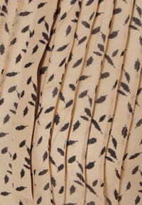 Tessuto beige con una texture plissettata, caratterizzato da un motivo ripetuto di foglie nere. La superficie appare morbida con una leggera lucentezza.