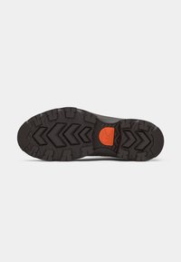 Semelle de chaussure de randonnée noire avec un motif de bande de roulement rugueux, un logo accent orange et une surface texturée pour une meilleure adhérence et traction.