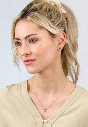 Gold chain necklace with green gemstone accents, worn with a light green blouse, featuring a round neckline and subtle texture.