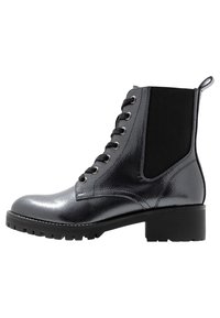 Botín negro hasta el tobillo con un acabado de cuero texturizado y brillante, paneles laterales elásticos y un tacón ancho. Presenta ojetes metálicos y cordones negros.