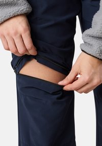 Navy trousers with a zippered opening at the knee. The fabric appears sleek and durable, with a soft grey fleece sleeve detail.