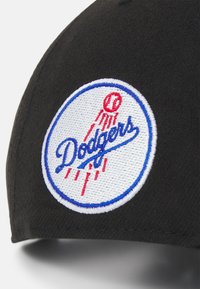 Black cap featuring a circular embroidered Dodgers logo in blue and white, with red accents and a textured fabric finish.