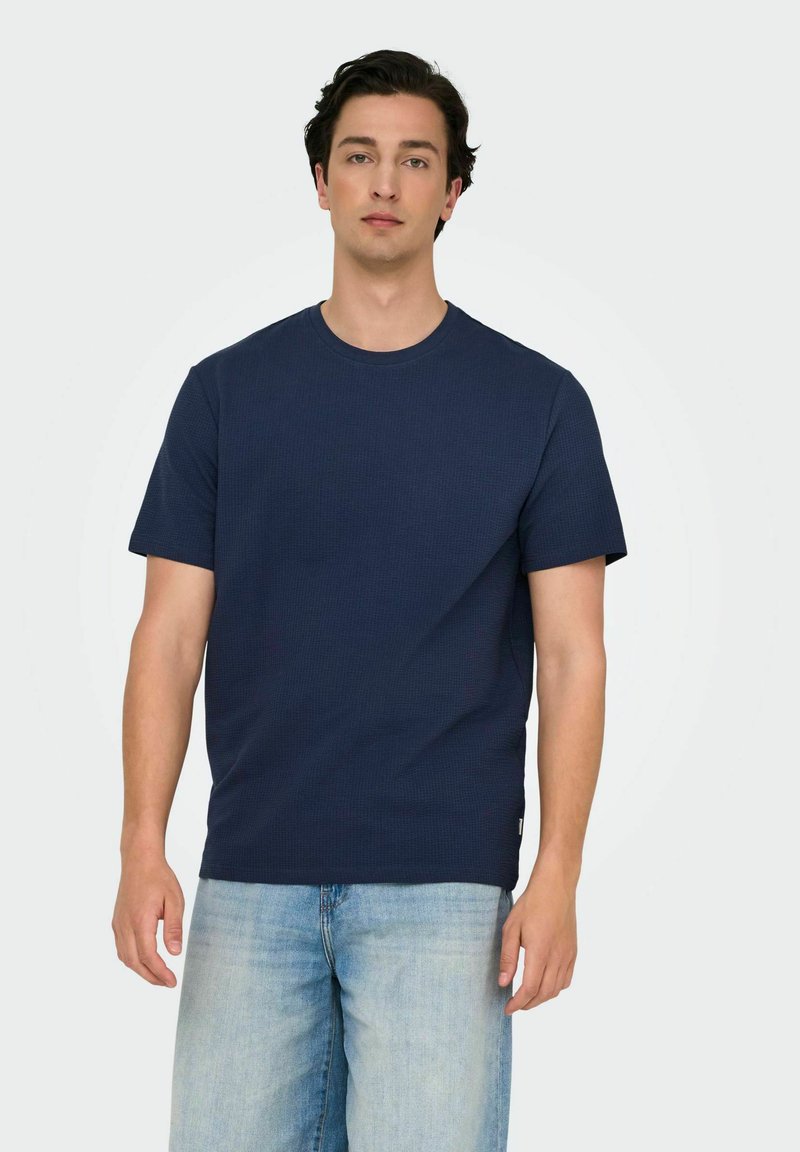 Mørkeblå kortærmet t-shirt med rund halsudskæring, tekstureret stof og en afslappet pasform; båret sammen med lyseblå denimjeans.