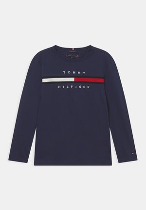 T-shirt bleu marine à manches longues en coton, arborant le logo "TOMMY HILFIGER" ainsi que des rayures rouges, blanches et grises sur la poitrine.