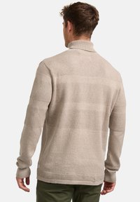 Beige kötött pulóver magas gallérral, textúrált vízszintes csíkokkal és bordázott mandzsettákkal. Az anyag puhanak és melegenak tűnik.