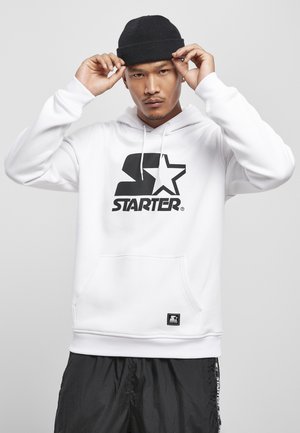 Hvid hoodie med et stort sort "Starter" logo og stjerned grafik. Har en frontlomme, snore og ribbede manchetter. Bæres med sorte bukser.