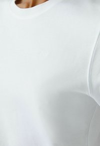 Witte katoenen t-shirt met ronde hals en subtiele geborduurde logo op de borst. Soepele textuur en fitted ontwerp, met minimale naden.