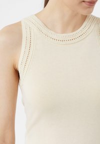 Beige mouwloze top met een gehaakte halslijn, met een gladde textuur en een aansluitende vorm. Eenvoudig ontwerp zonder extra patronen.