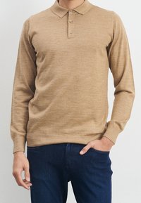 Beige polo shirt met lange mouwen, gemaakt van een gestructureerde brei, met een drieknoopsluiting en ribgebreide manchetten en zoom, gecombineerd met donkerblauwe jeans.