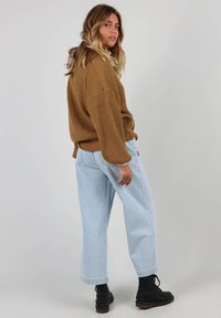 Un pull brun à côtes, avec des épaules tombantes et un pantalon en jeans large bleu clair, associé à des bottes à lacets noires, vu de dos.