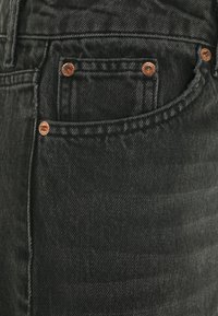 Tummanharmaat farkut, joissa on teksturoitu kangas, kupariset niitit etutaskussa ja näkyvä sauma alasivussa.