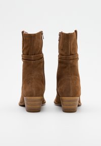 Bruna mockaankelboots med en lätt slouchad design, dragkedja och en staplad träklack. Har perforerade detaljer på ovansidan.