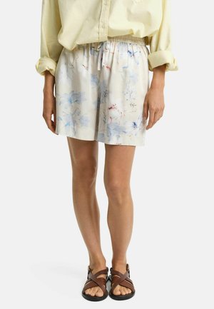 Blumen-Shorts aus weichem Stoff mit einem elastischen Bund, in sanften Farben und dezenten blauen und rosa Mustern, kombiniert mit braunen Sandalen.