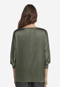 Olivgrön satintopp med rak skärning, trekvarts puffärmar och en bred halsringning. Slät textur med minimal detaljering.