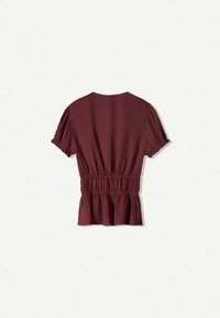 Blusa bordeaux a maniche corte con vita arricciata e stile peplum. Realizzata in tessuto leggero e texturizzato con scollo rotondo.