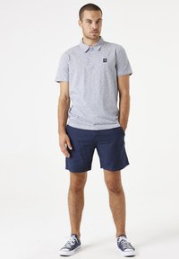 Polo gris a rayas con cuello, mangas cortas y un pequeño logo; combinado con pantalones cortos azul marino y zapatillas azules. Diseño simple.
