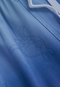 Helle blaue Badehosen mit einem dezenten Schildkrötenmotiv, aus einem glatten, schnell trocknenden Material mit weißen Kordelzug-Akzenten.